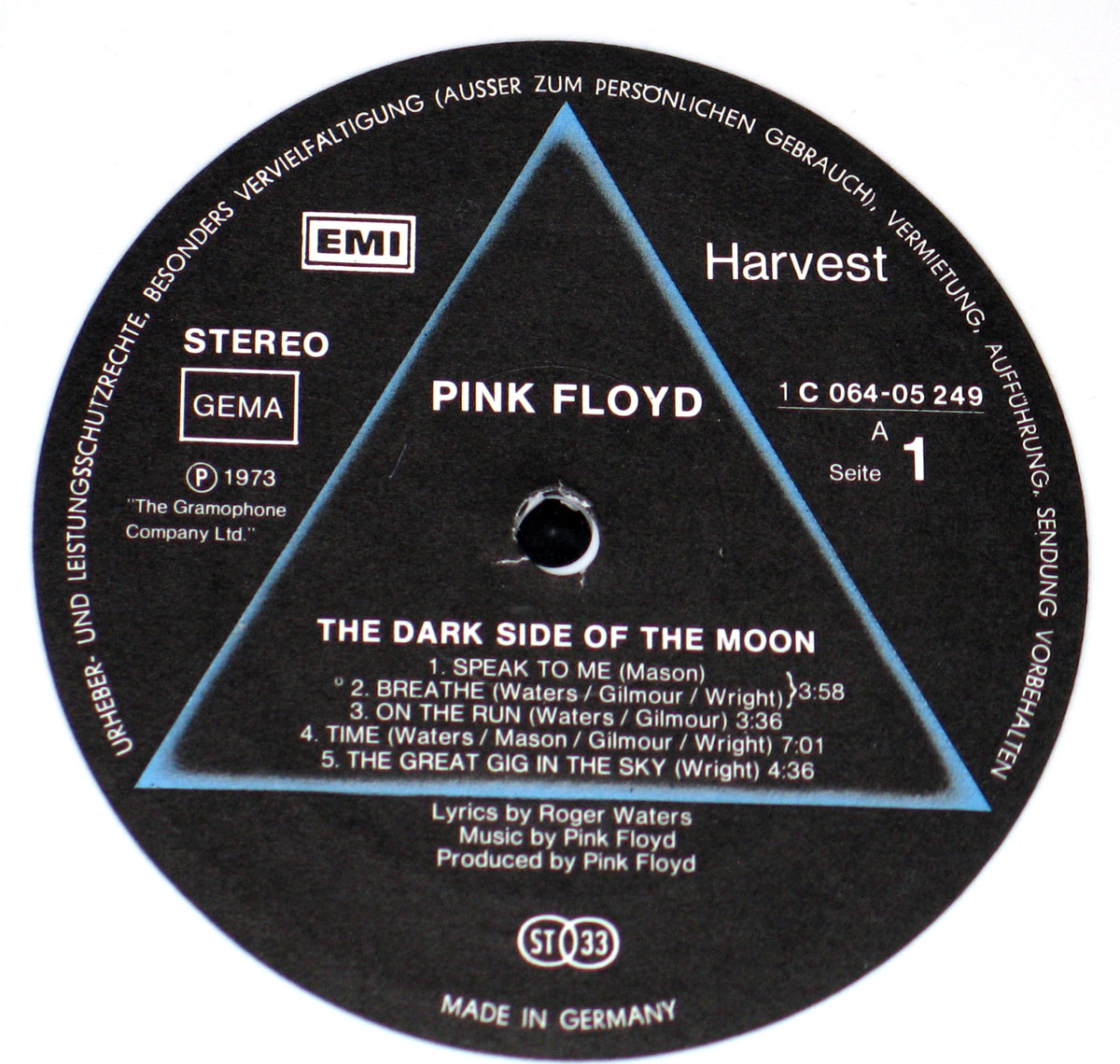 ‘Record label for Side A of Pink Floyd’s The Dark Side of the Moon, featuring a black background with a central triangle design. The label includes the Harvest and EMI logos, German copyright text around the edge, track listings, and credits for Roger Waters and Pink Floyd. The catalog number “1 C 064-05 249,” GEMA rights mark, “ST 33” stamp for stereo 33 1/3 RPM, and “Made in Germany” are also displayed.’